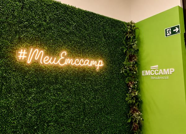 Letreiro em neon #MeuEmccamp sobre parede de folhagem