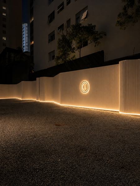 Muro de entrada com logotipo iluminado e faixa de luz, à noite